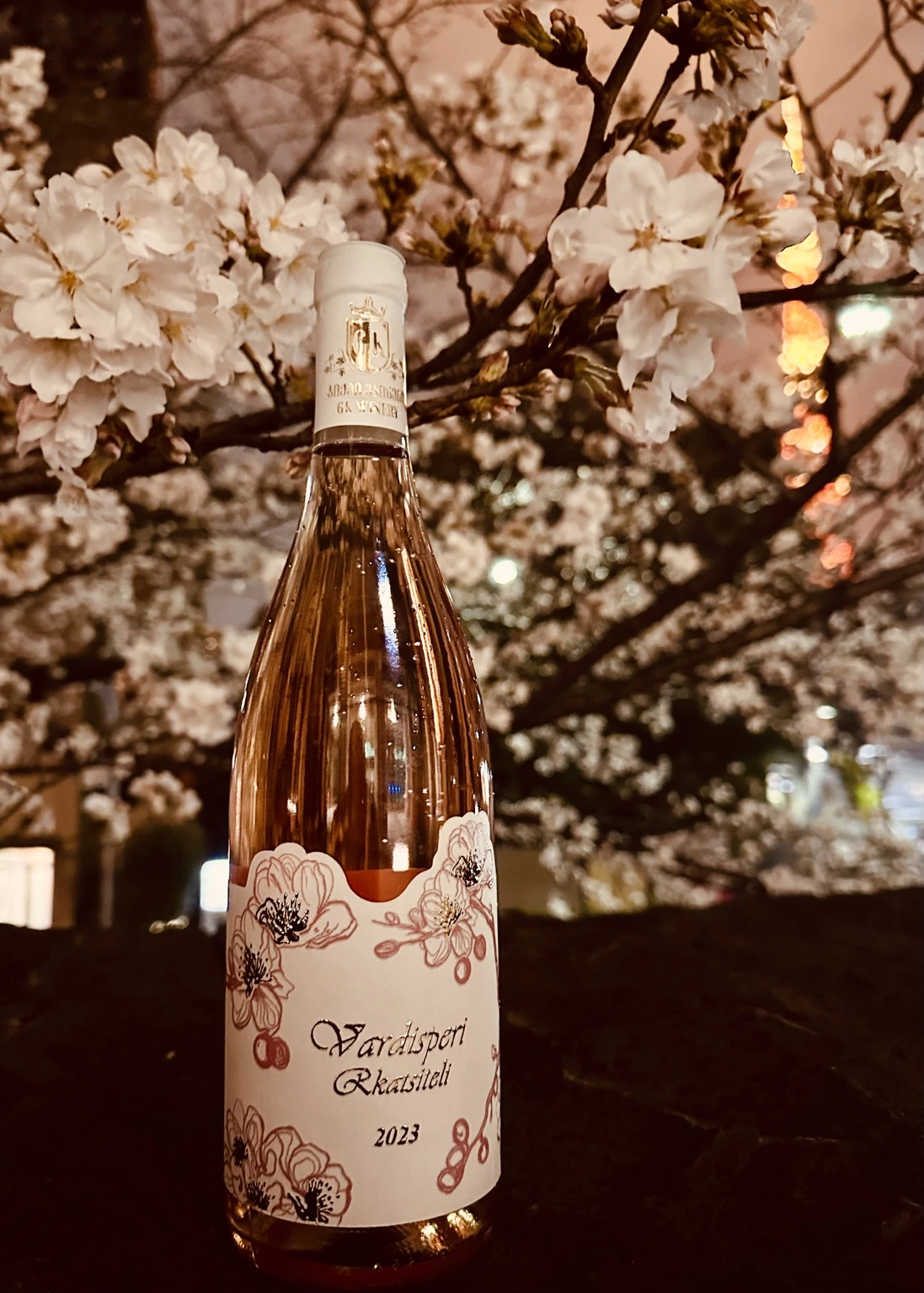 Vardisperi Rkatsiteli bottle among cherry blossoms at night